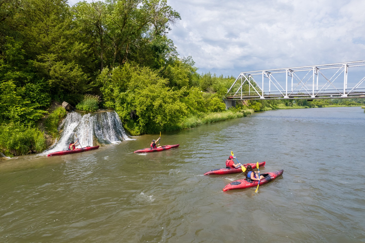 Four kayakers paddle past a waterfall towards a bridge on the Niobrara River near Valentine.