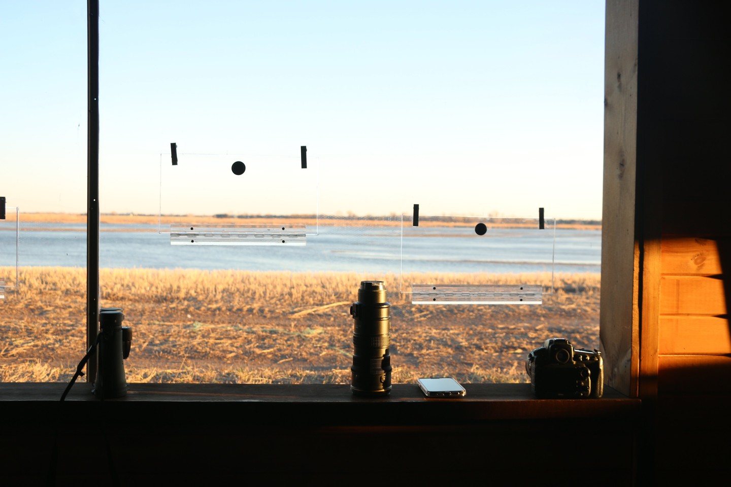 Binoculars, cameras and lenses on a window sill looking out on the river for sandhill cranes at Crane Trust.