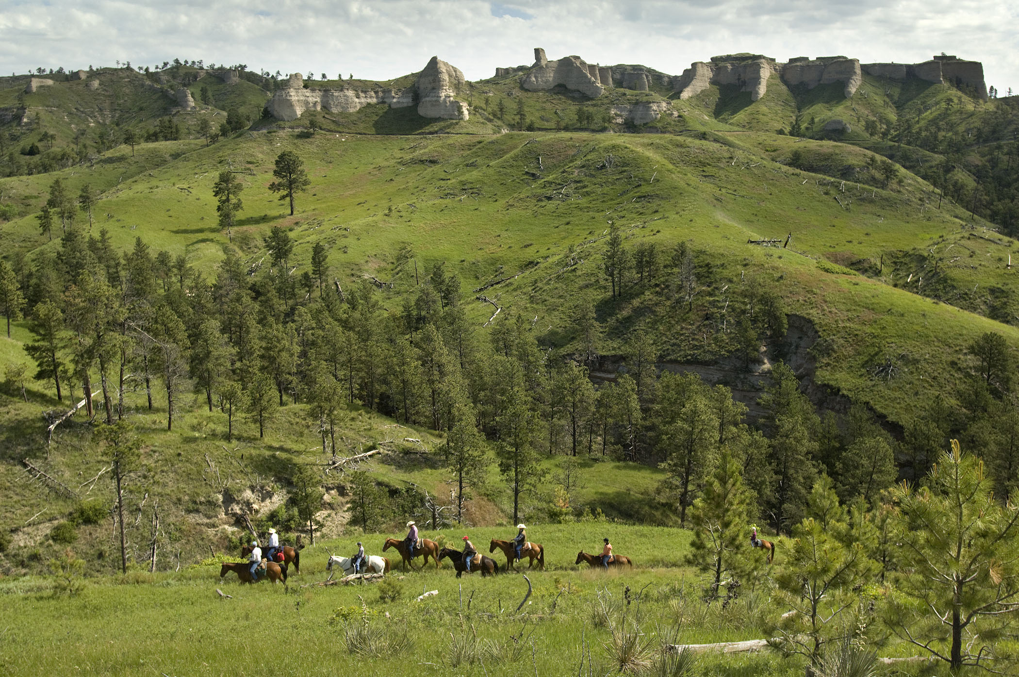 Horsback riders on a trail beneath a massive ridge at Fort Robinson State Park.