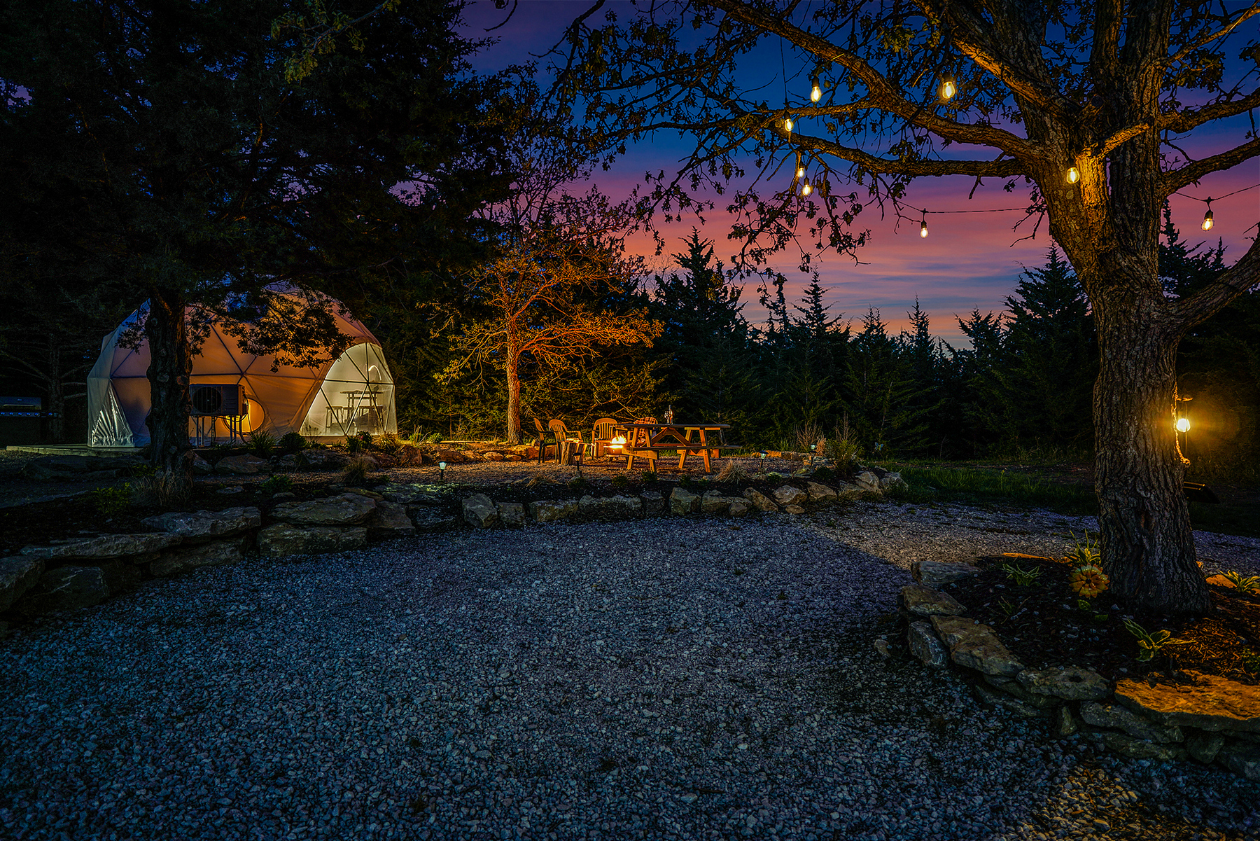A tree with lighting in gravel near fire pit and chairs next to a geodesic dome at sunset at Kimberly Creek Retreats. 
