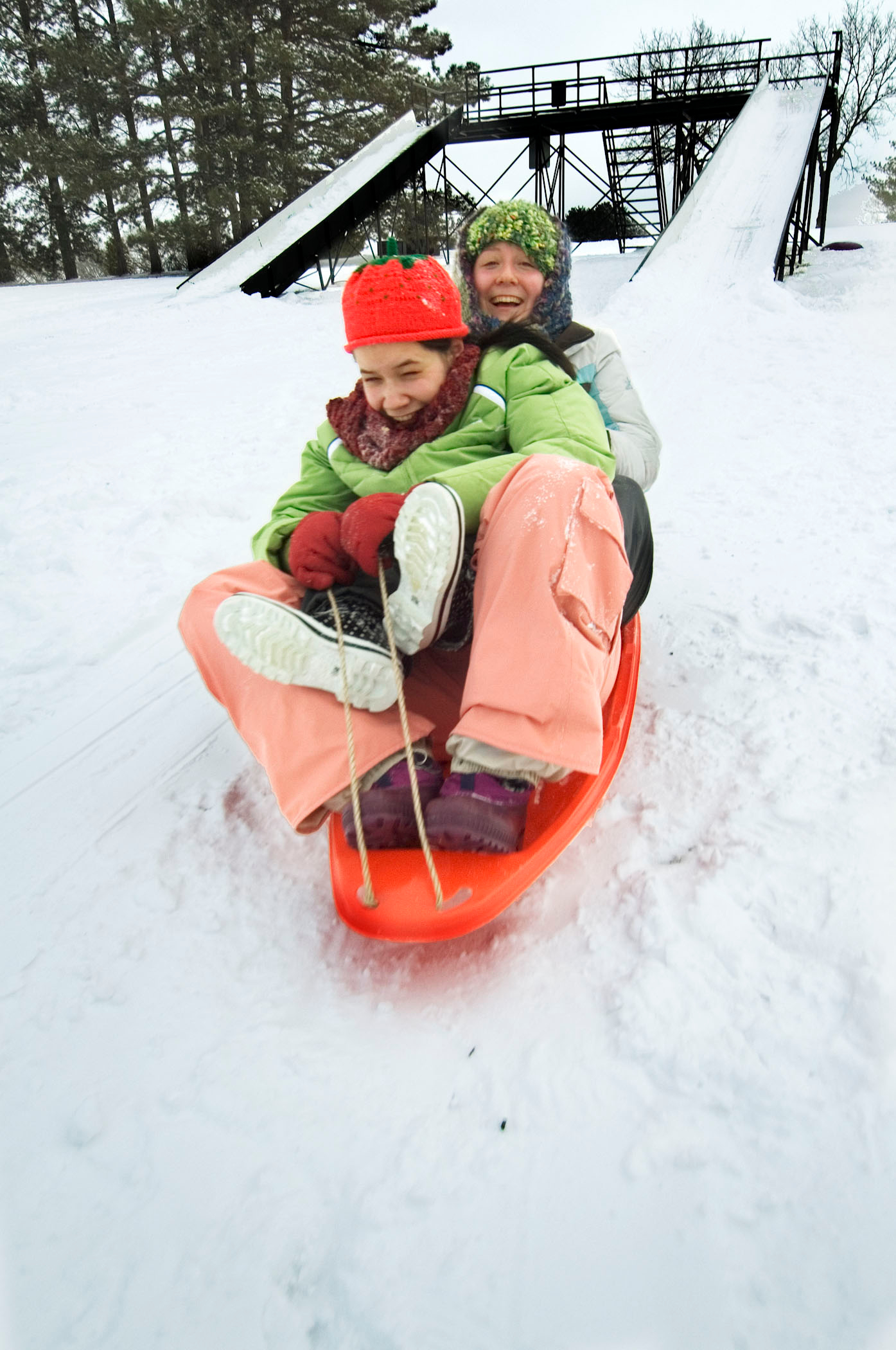 Two people sledding on an orange sled at snowy Pioneers Park in Lincoln.