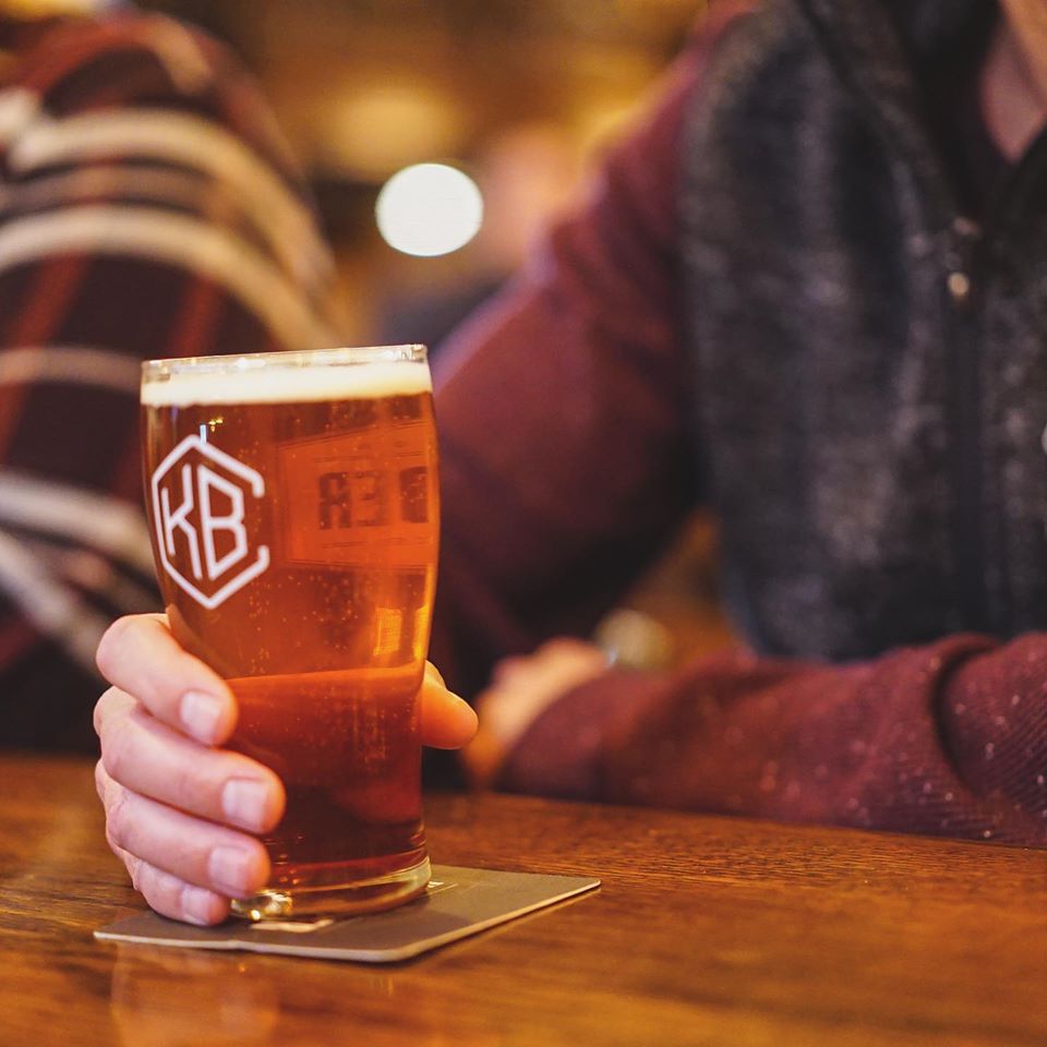 Someone holding a beer glass at the bar at Kinkaider Brewing Co.