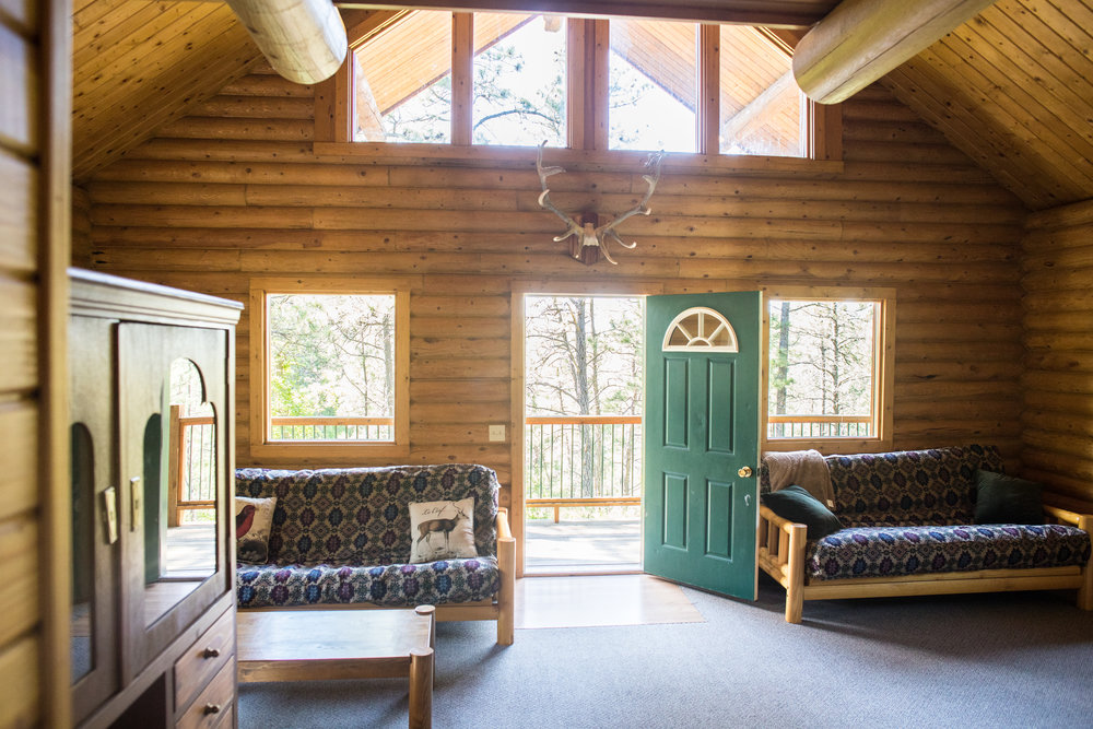Inside the Stone House Cabin at Heartland Elk Guest Ranch with wood furniture around the room and antlers above the door.
