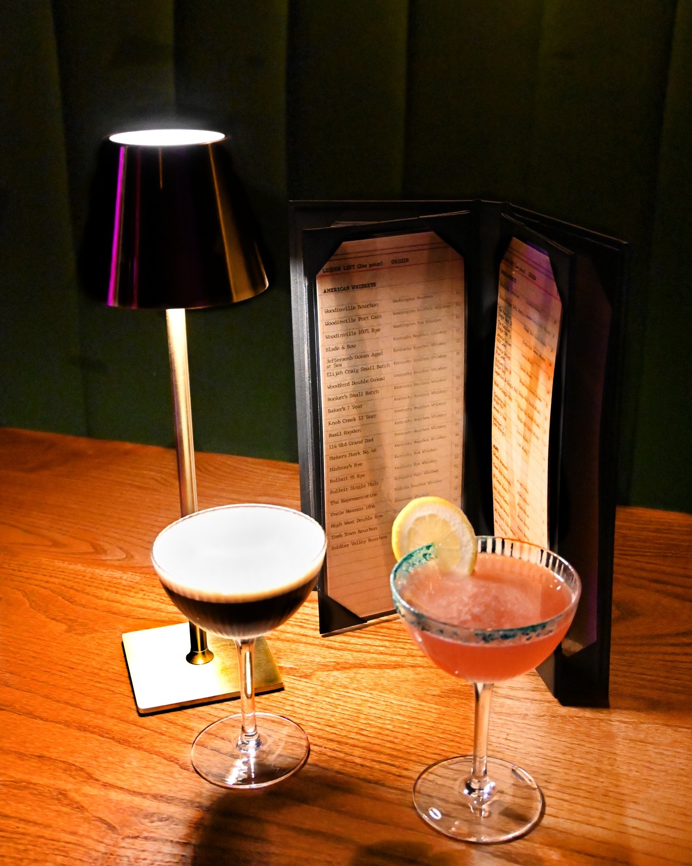 Two cocktails in front of a lamp and drink menu at The Vault in Omaha