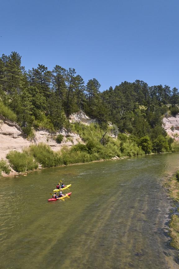 Kayakers on the Niobrara River surrounded by bluffs and greenery. 