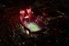 A sold out Memorial Stadium at night with red fireworks overhead during a home Nebraska Huskers football game.